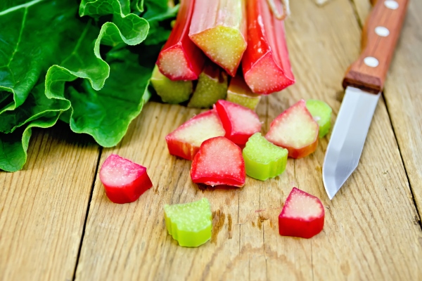 bundle of stalks of rhubarb cut pieces of rhubarb with a leaf and a knife on a wooden board - Орловский ревеневый квас
