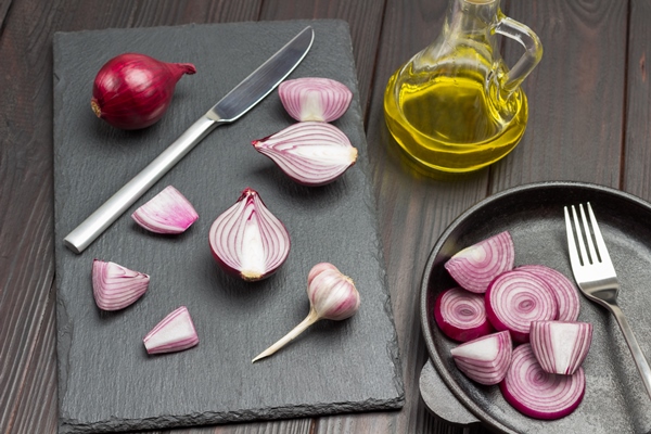 chopped onion knife and one whole onion on cutting board chopped onions and fork in frying pan oil bottle dark wooden background top view - Суп с рисом и капустой