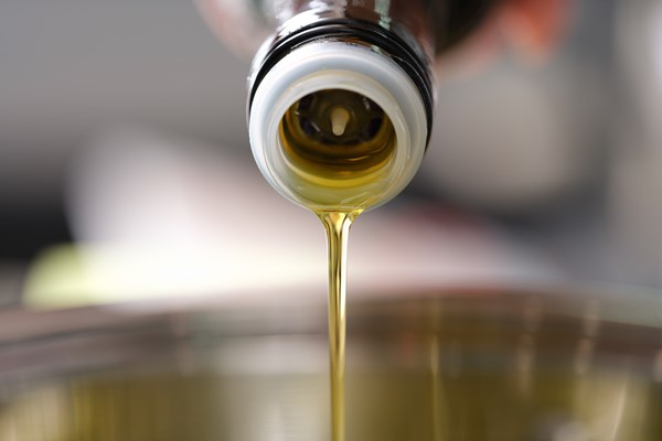 clear olive oil is poured from dispenser bottle into saucepan cooking in vegetable oil concept - Деруны без яиц