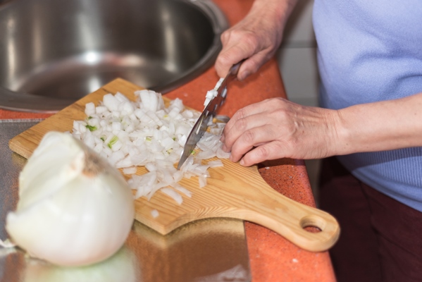 close up view of senior woman hand cutting onion shallow dof selective focus on the hand - Суп-пюре из гороха с гренками