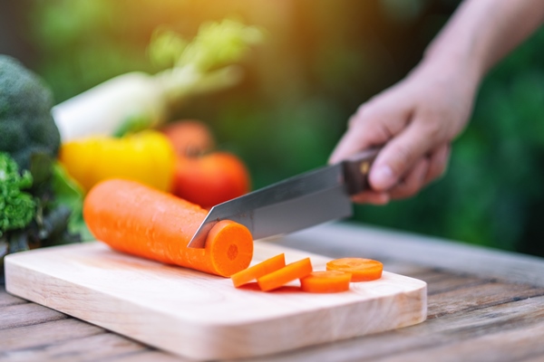 closeup image of a hand cutting and chopping carrot by knife on wooden board - Суп с зелёным горошком