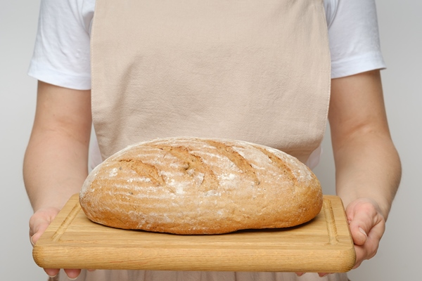 closeup of a girl in a beige apron holding a loaf of homemade bread in her hands on a cutting board space for text mockup copy space - Бездрожжевой гречневый хлеб