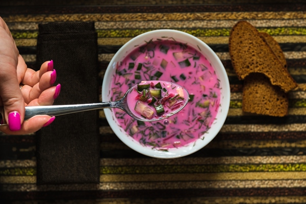 cold beetroot soup on a spoon in your hand and bread on a decorative tray soup kholodnik red on an unusual tray food - Холодник