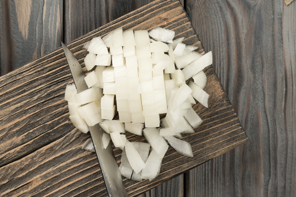 cutting white spicy onion with knife into cubes on kitchen wooden board white diced onion flat lay view healthy food - Щи зелёные из молодой крапивы