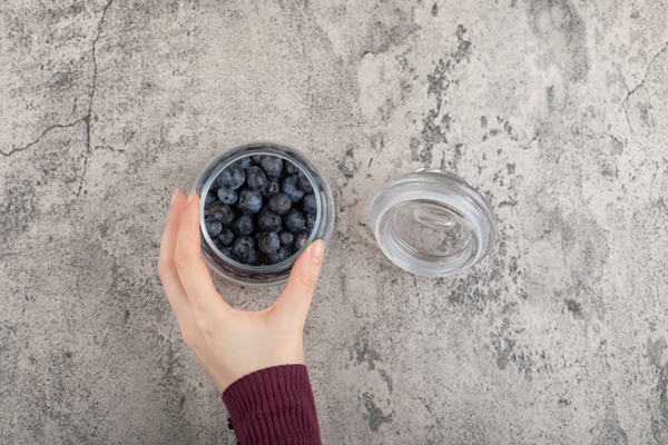 female hand holding glass of fresh blueberries on marble surface - Натуральная черника в собственном соку