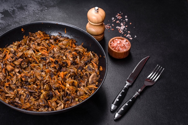 fried champignons with carrots onions and spices in a pan against a dark concrete background - Щи из квашеной капусты с грибами