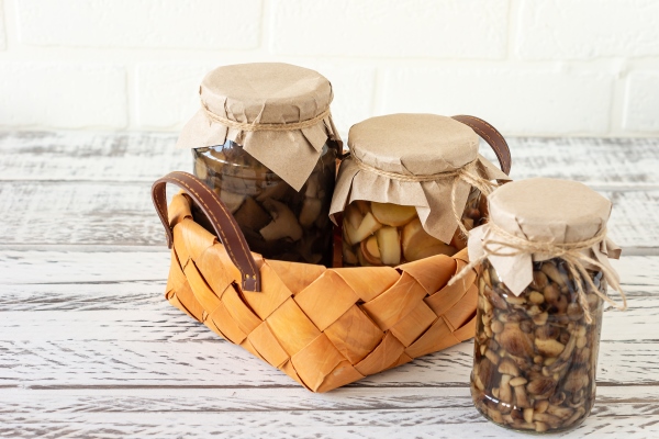 glass jars with canned mushrooms in a basket fermented food on a white background with copy space - Окрошка со сливами