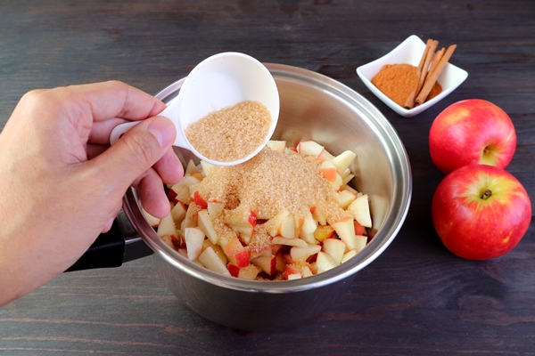 hand adding unrefined sugar into the pot of diced apples for making a healthy compote - Курский квас яблочный