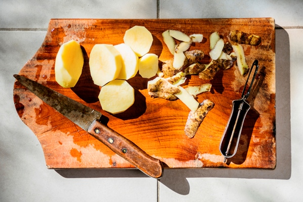 high angle view of sliced potatoes with knife on wooden cutting board - Рассольник с рисом