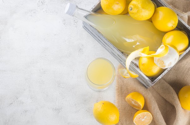 limoncello in glass bottle and fresh ripe yellow lemons on the grey background traditional homemade sweet italian lemon liqueur strong alcoholic drink and fresh ripe yellow lemons - Госпитальный квас