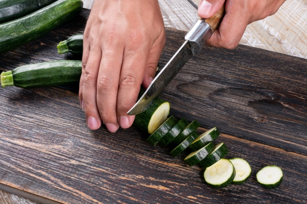 man cutting fresh zucchinis into slices on a cutting board on a wooden table - Гороховый суп с кабачками