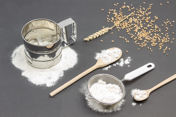mug for sifting flour and small sieve with flour wheat spikelet wooden spoon and wheat grains on table - Домашний хлеб на сухих дрожжах