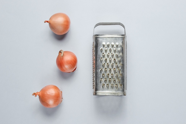 old grater and onion bulbs on gray surface - Драники с морковью и луком