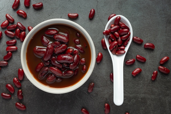 red bean boiled in white bowl with red bean seed in spoon place on dark floor - Суп острый из красной фасоли с орехами