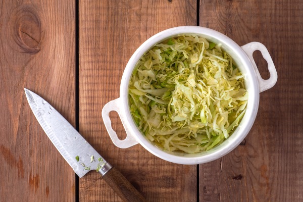 salad preparation finely chopped fresh cabbage in a white plastic saucepan on a wooden table - Суп из свежих помидоров с капустой