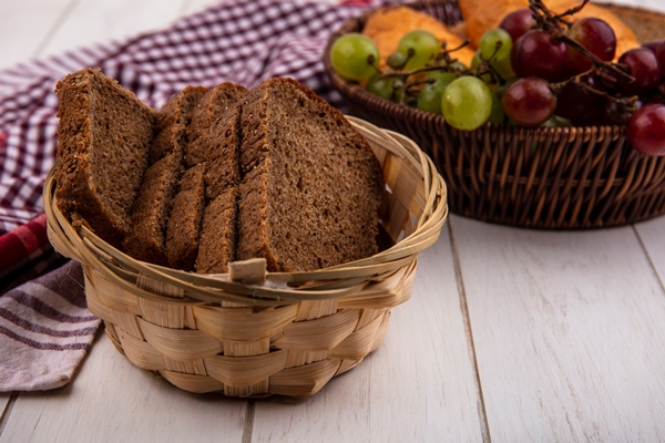 side view of rye bread slices in basket on plaid cloth with basket of grapes nectacots on wooden background - Квас с корицей (украинская кухня)