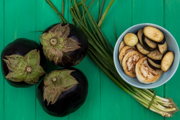 top view green onion with eggplant and slices in a plate on green background - Постный суп из чечевицы с баклажанами