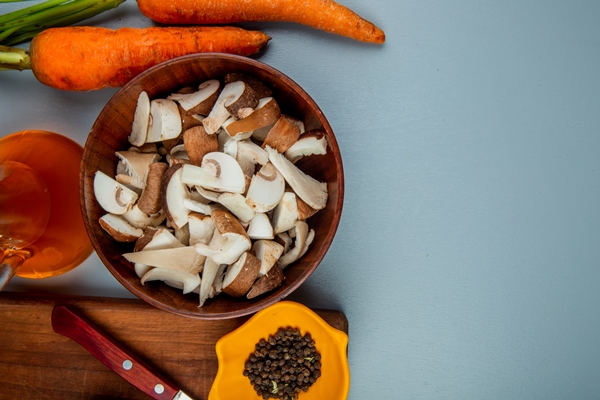 top view of fresh sliced mushrooms in a bowl and kitchen knife with black peppercorns on a wood cutting board and fresh carrots on light blue with copy space - Щи зелёные из молодой крапивы