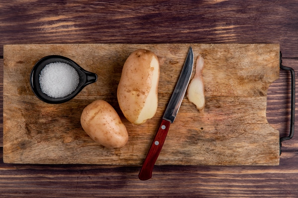 top view of potatoes salt knife on cutting board on wood - Драники с яблоками и брусникой