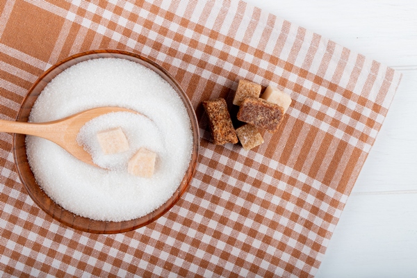 top view of white sugar in a wooden bowl with a spoon and lump sugar and palm sugar pieces on plaid tablecloth with copy space - Черника протёртая с сахаром