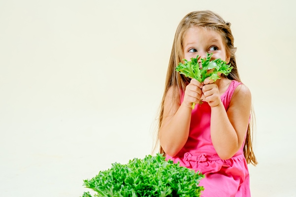 beautiful little girl with lettuce in hand on a light monophonic background proper nutrition - Зелёный салат со сметаной и яйцом