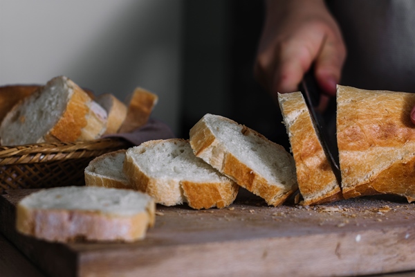 close up of a baker s hand slicing loaf of fresh bread - Греночки из белого хлеба