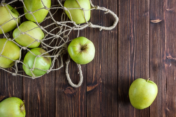 green apples in a net bag and around top view on a wooden background - Яблочные цукаты