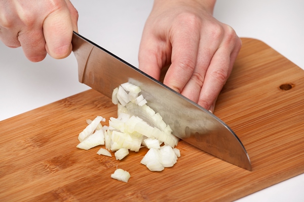 hand with a kitchen knife cuts and chops onions on a wooden cutting board - Постный соус чатни из яблок