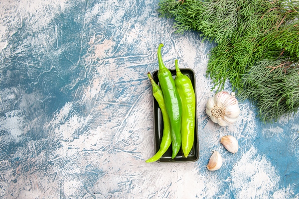 top view green hot peppers on black plate garlic on blue white background - Постная яблочная острая аджика