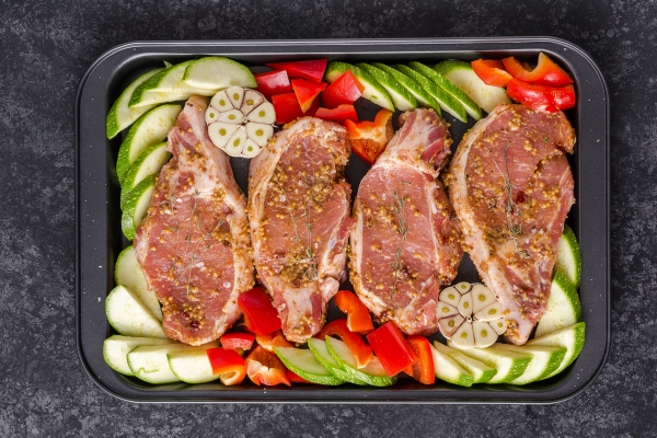 uncooked pork steak with bell peppers and zucchini on baking tray for roasting - Жареное мясо