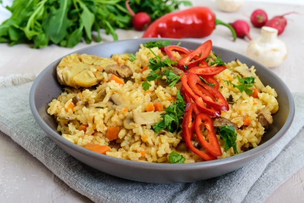 a traditional asian dish pilaf with meat mushrooms and pepper capi in a bowl - Грибной постный плов
