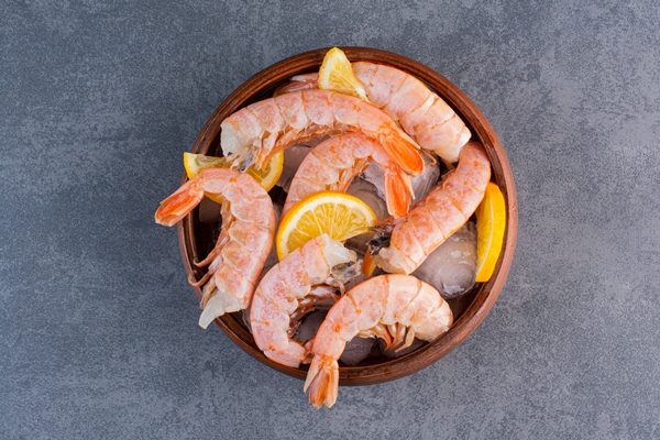 a wooden plate of delicious shrimps with ice cubes and sliced lemon on a stone surface - Цветная капуста с креветками, постный стол