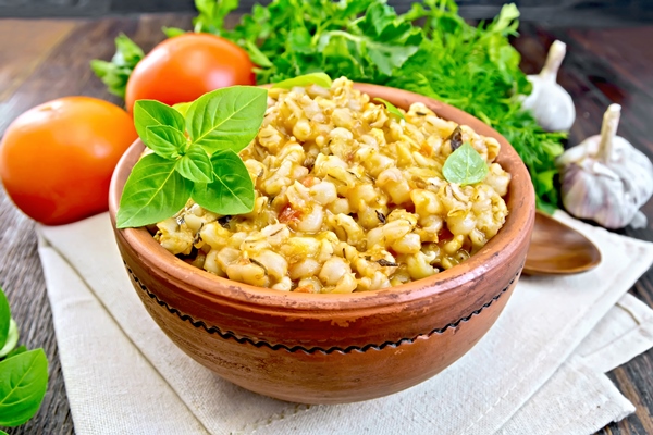 barley porridge in a clay bowl with basil on towel tomatoes parsley and garlic on a wooden boards background - Перловая каша с постным маслом