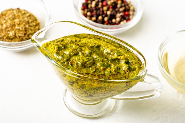 chimichurri sauce in a gravy bowl on a white background various spices lie nearby argentinean vegetarian sauce made from olive oil oregano parsley - Постный соус "Чимичурри"