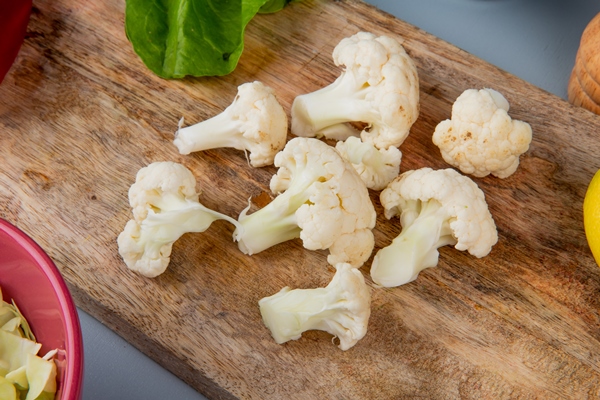 close up view of cauliflower pieces with spinach on cutting board and cabbage slices on blue background - Цветная капуста с креветками, постный стол