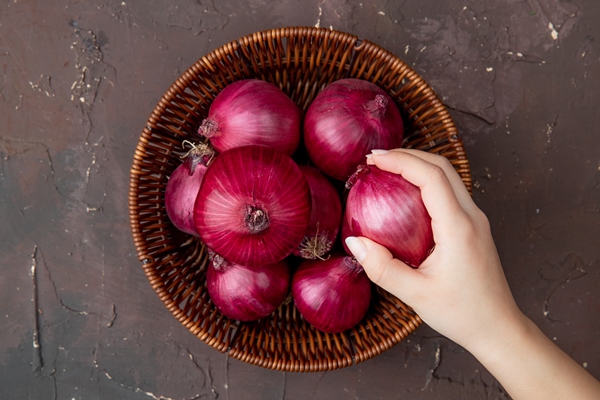 close up view of woman hand holding onion and basket of onions on maroon background with copy space - Постный огуречный соус с луком