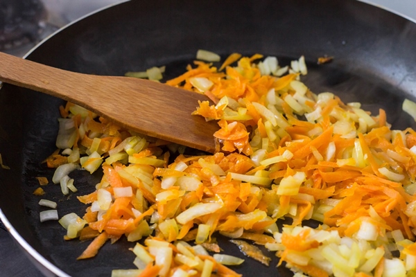 crushed onions and carrots in a frying pan and wooden spatula - Постная лазанья с чечевицей