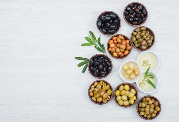 different kinds of olives and olive oil in a clay and white bowls with olive leaves flat lay on white wood - Салат из нута со сладким перцем