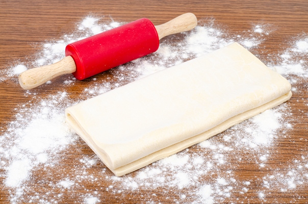 folded plate of raw dough with flour on wood table - Пирожки из слоёного теста постные