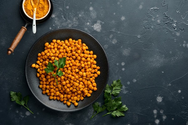 fried chickpeas with turmeric with parsley and lime in black plate on an old black table background roasted spicy chickpeas or indian chana or chole popular snack recipe top view - Салат из нута со сладким перцем