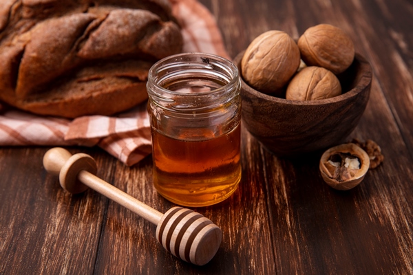 front view honey in a jar with walnuts and a loaf of black bread on a wooden background - Тыква с яблоками и мёдом