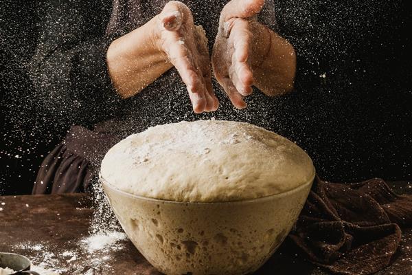 front view of female chef dusting her hands with flour before handling pizza dough - Голландские пончики (oliebollen)