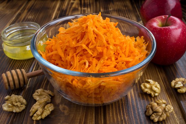grated carrot in the glass bowl and ingredients for salad on the brown wooden - Салат из моркови и яблок с сахаром и мёдом