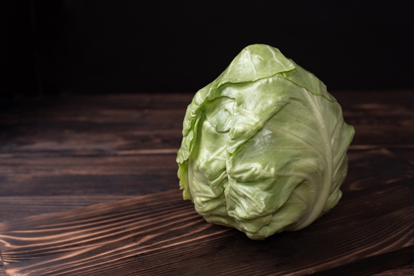 head of early cabbage on a cutting board on a dark wooden background - Постная тушёная капуста с яблоками