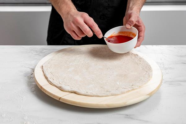 high angle man spreading tomato sauce on pizza dough - Постная пицца с грибами и овощами