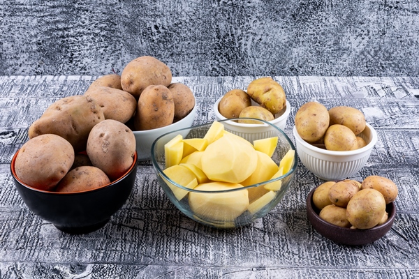 high angle view small chopped and big potatoes in bowls on gray wooden table - Гороховый суп с томатом