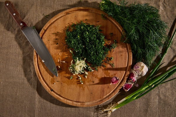 overhead view of a bunch of fresh moist dill on a linen tablecloth and garlic next to a wooden cutting board with a kitchen knife and chopped garlic and dill seasonal greens food background flat lay - Постный майонез с огурцами