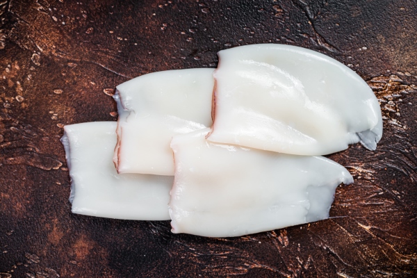 raw squid or calamari tubes on a kitchen table dark background top view - Кукурузный салат с морепродуктами постный