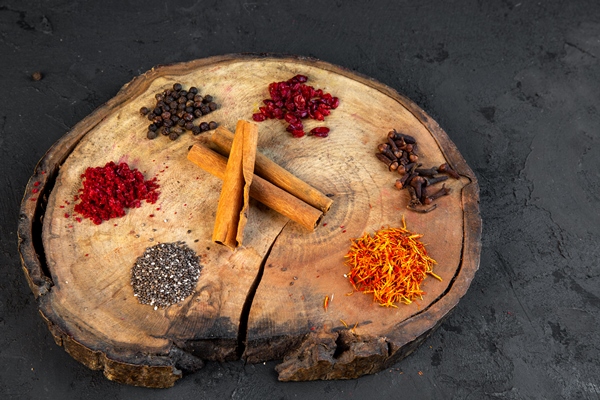 side view of various spices saffron chili powder black pepper and cinnamon sticks on round wooden board - Рисовая каша с пряностями и орехами