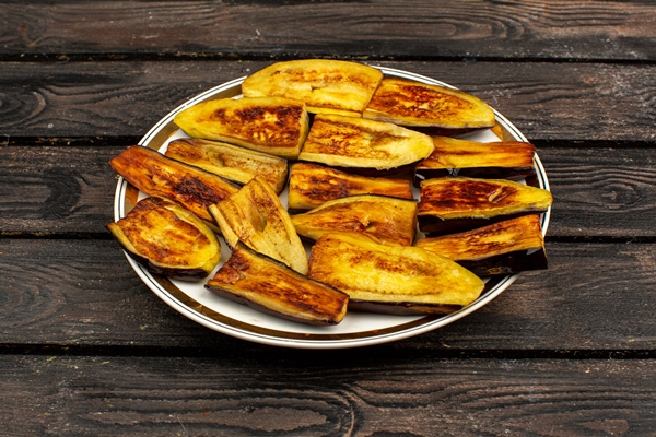 sliced eggplants fried tasty on a round plate and rustic wooden desk - Баклажанные рулетики с морковью